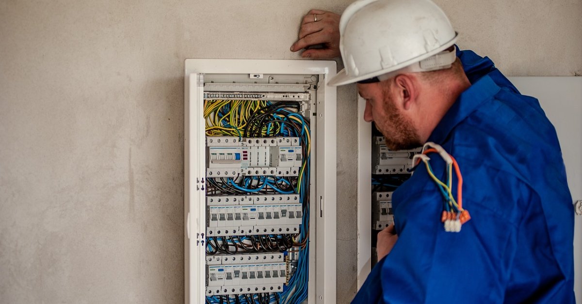Monteur in blauwe werkkleding inspecteert een open elektrische schakelkast.