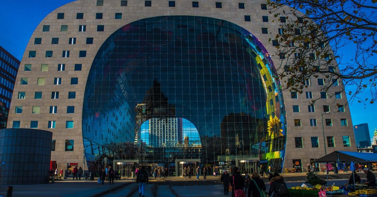 De grote boogvormige gevel van de Rotterdamse Markthal met glazen middenpartij en bezoekers op het plein.